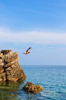 Boy Jumping Off Cliff Into Blue Water at sunset