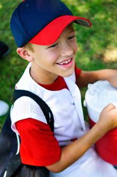 Little league baseball player happy after the game about to drink some water.