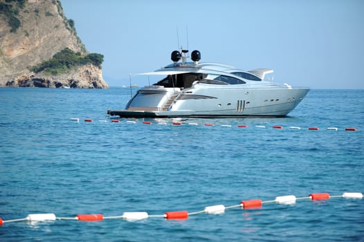 A luxury silver motor yacht on the sea with coast in the background, reef in the Montenegro