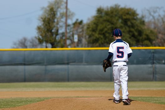 Little league baseball player taking the mound to pitch.