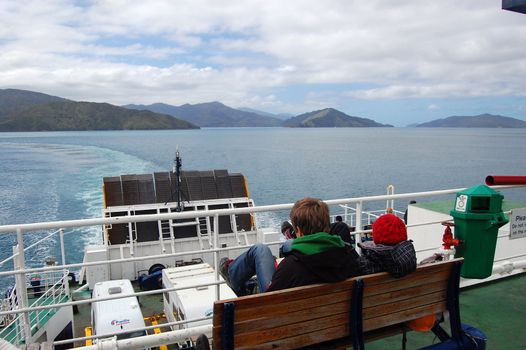 People sit on ship bench, between South andNorth Island, New Zealand