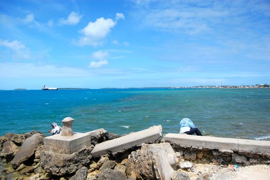 People sit at ocean coast, Tonga capital town