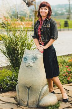 Young woman standing near funny cat statue in summer day