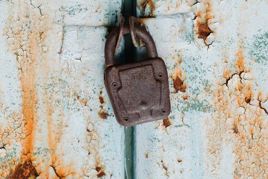 Old padlock on rusty metal painted door