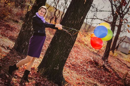 Young pregnant woman with colorful balloons in autumn forest