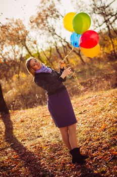 Young pregnant woman with colorful balloons in autumn forest
