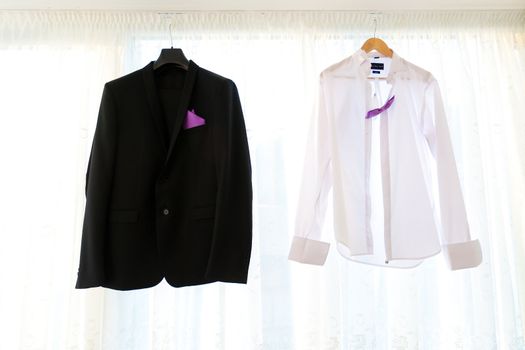 Suit jacketand shirt hanging on a hanger with purple bowtie 