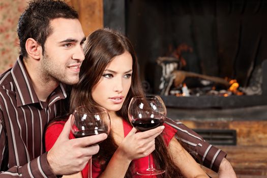 Young couple in love enjoying wine near fireplace