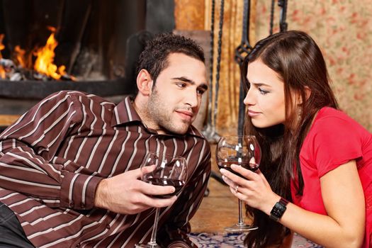 Young couple in love near fireplace holding glass of wine, focus on woman