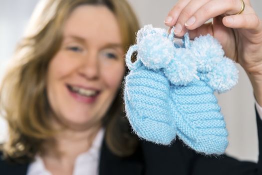Blond woman is holding two blue baby shoes