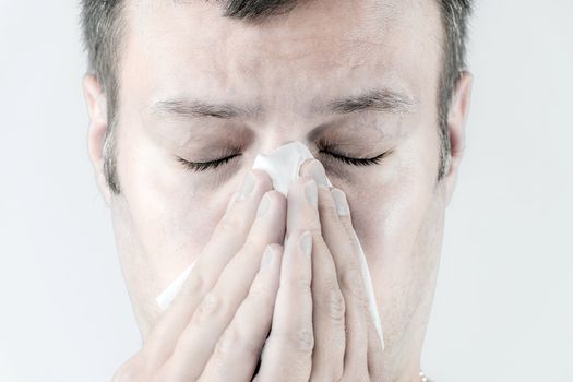 Portrait of a ill man who is sneezing in a tissue