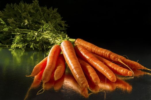 A bunch of carrots with greens and dark background