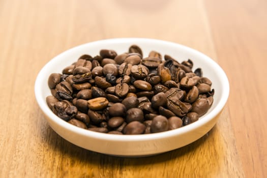 Small white cup of coffee beans on a wooden table