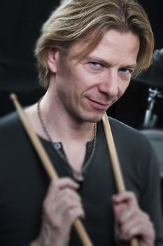 Man in front of a black background an his drums is holding drumsticks and is looking to the viewer