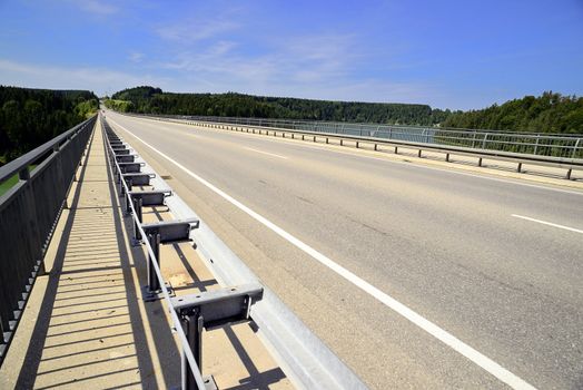 Concrete road bridge over the river called "Lech". Placed in Germany, Bavaria, Allgäu. There are also coniferous trees and blue sky, sunny weather.