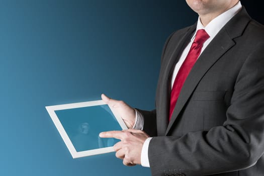 Well dressed business man is holding a tablet computer. Background is blue / black.