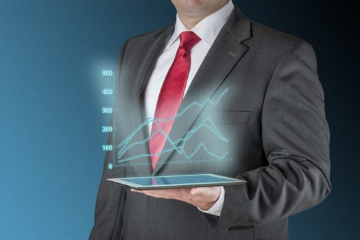 Well dressed business man is holding a tablet computer that is showing a stock chart. Background is blue / black.