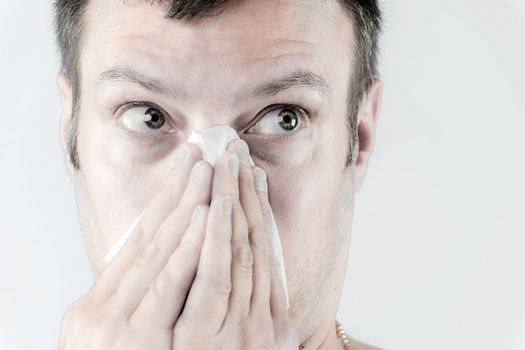 Portrait of a ill man who is sneezing in a tissue