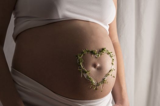 Young woman with white clothes and a cream and cress heart on her baby bump