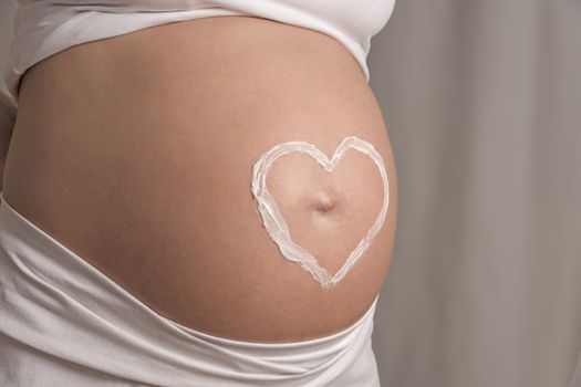 Young woman with white clothes and a cream heart on her baby bump