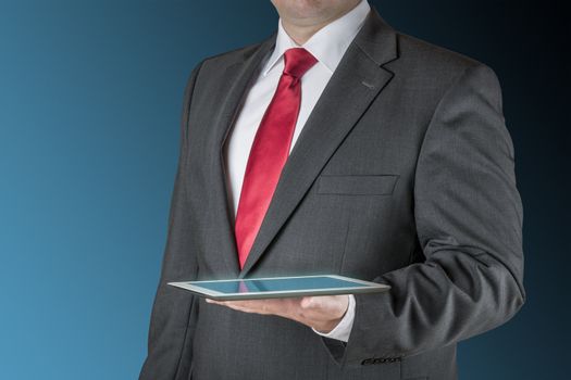 Well dressed business man is holding a tablet computer. Background is blue / black.