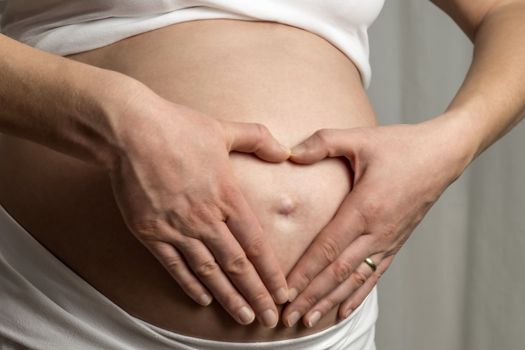 Close up of a baby bump with holding hands like a heart