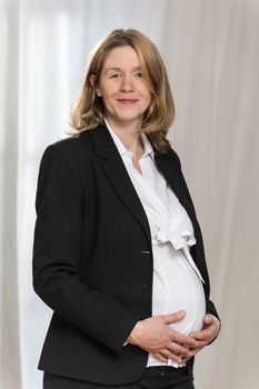 Pregnant blond business woman in black business clothing with light background is looking to the viewer