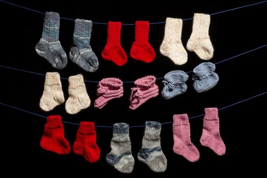 Blue, red, pink and white babysocks on a line in front of a black background