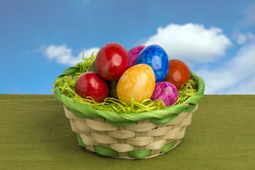 Easter basket with colored eggs, blue sky and white clouds
