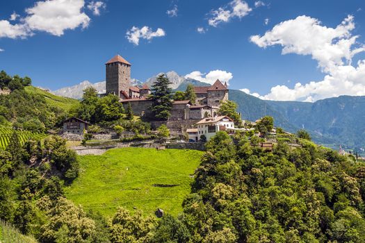 Tirol castle on a sunny summer day with blue sky, white clouds, green meadows and trees