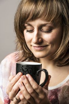 Young woman enjoying tea or coffee in a black cup