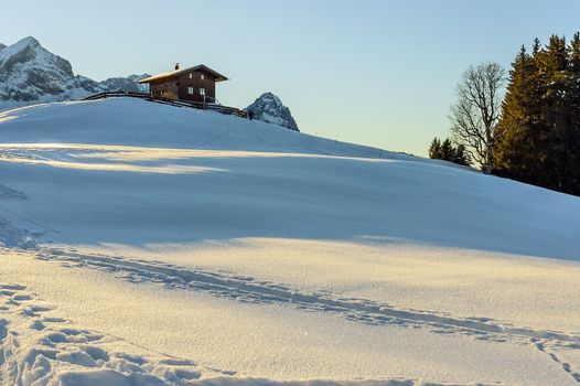 Alp landscape with wooden cabin in alps with prints in snow and sunset in Germany December