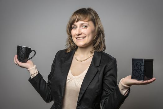Young brunette woman with black clothes holding a black cup and a black tea tin