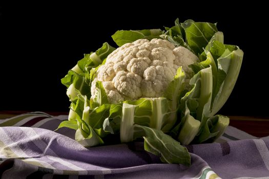Cauliflower with green leaves on a dish towel and dark background