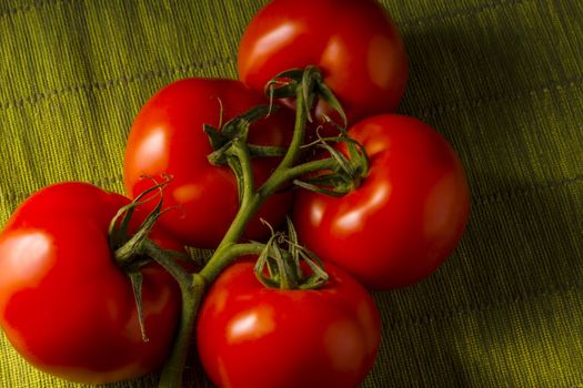 Five red tomatoes on a green tablecloth