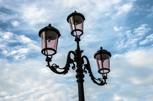 Cast iron street lamp in Venice in front of blue sky with clouds