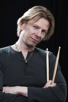 Man in front of a black background an his drums is holding drumsticks