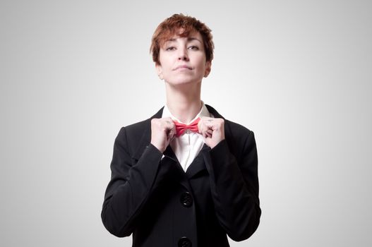 elegant businesswoman adjusting bow tie on gray background