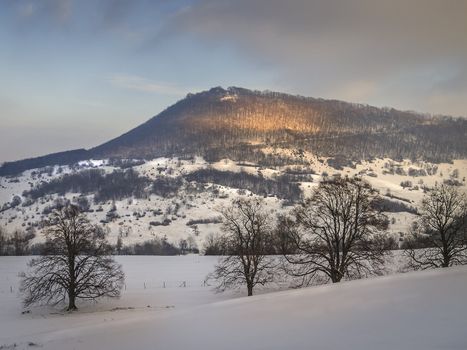 Winter landscape with snow, a hill, trees in evening mood