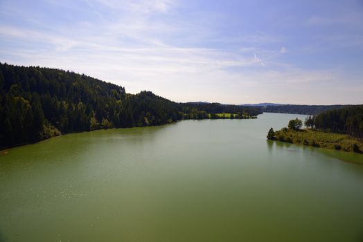 River with green colored water, woods and blue sky and white clouds on a summer sunny day.