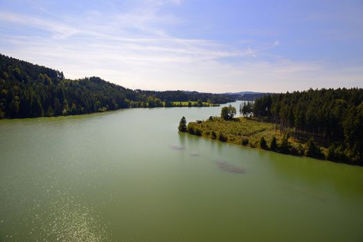 River with green colored water, woods and blue sky and white clouds on a summer sunny day.