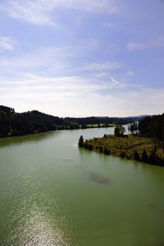 River with green colored water, woods and blue sky and white clouds on a summer sunny day.