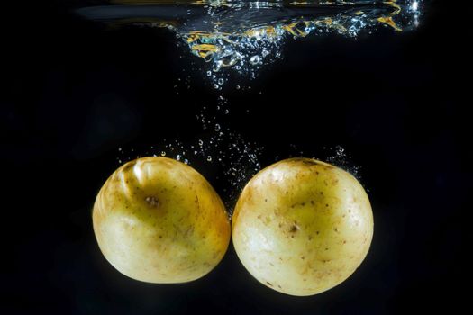 Two yellow potatoes under water with bubbles