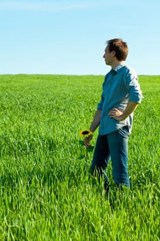 young man standing with a sunflower in the green field 