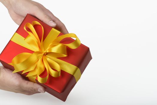 gift with gold ribbon in red paper on white underground holding in hands