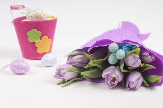 Easter eggs with bucket and tulips on light background
