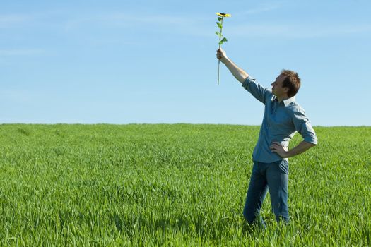 young man standing with a sunflower in the green field 