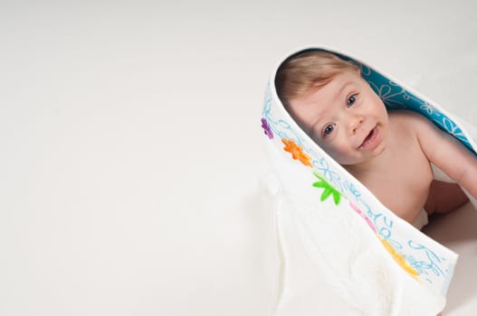 Happy little boy in white blanket with flowers in studio