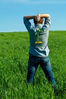 young man standing with a sunflower in the green field 