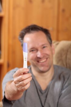Happy man smiling and holding a positive pregnancy test